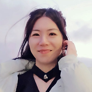 Dr. Jingyun Wang fotografuota lauke, ilgi tamsūs plaukai, vilki baltą striukę ir juodą palaidinę, &scaron;velni &scaron;ypsena.