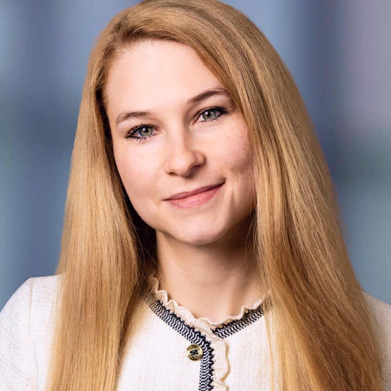 Dr. Lisa Bardach pozuoja studijos fone, ilgi šviesūs plaukai, vilki šviesią palaidinę su dekoratyviais nėriniais prie kaklo, švelniai šypsosi.