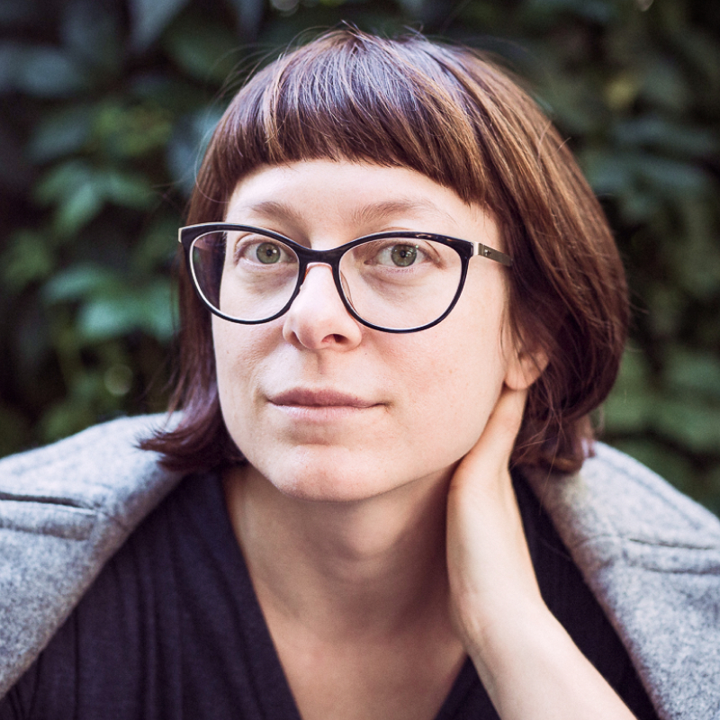 Dr. Rasa Erentaitė lauko aplinkoje žiūri į kamerą, trumpi rudi plaukai, dideli akiniai, atrama rankai po smakru.