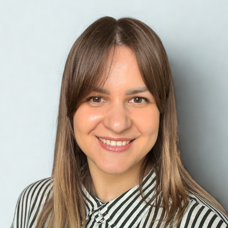 Kristina Šmaižienė šypsosi priešais šviesų foną, rudi plaukai ties pečiais, vilki baltą ir juodą dryžuotą palaidinę.